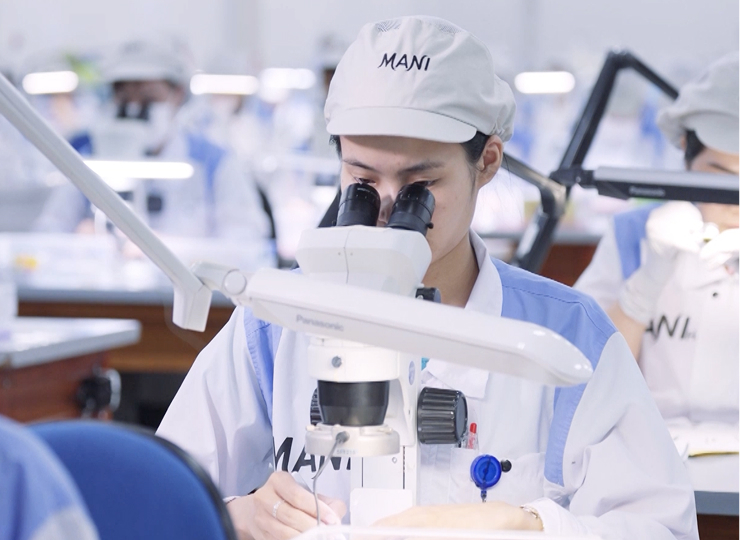 A technician in a MANI uniform carefully inspecting an item under a microscope in a clean, well-lit lab environment