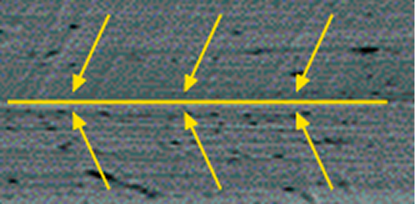 Microscopic image of suture needle surface showing smooth texture with directional alignment, indicated by yellow arrows