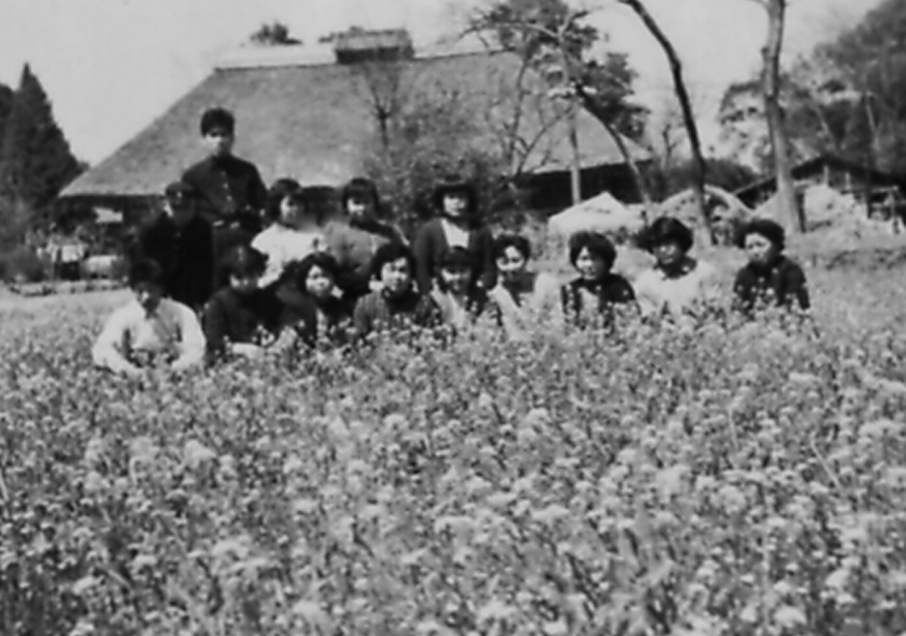 a group of individuals sitting in a field with traditional houses in the background