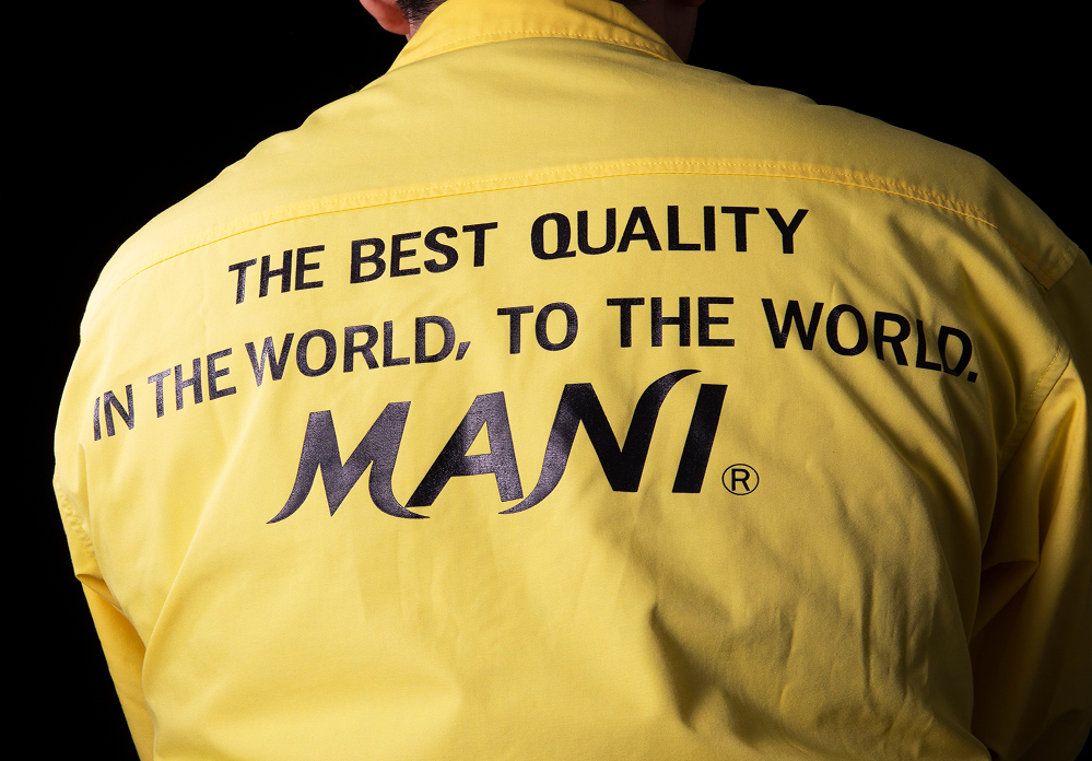 Back of a person wearing a yellow MANI jacket with the slogan 'THE BEST QUALITY IN THE WORLD, TO THE WORLD.