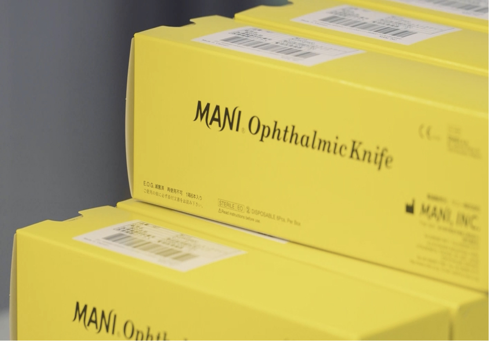 Stacked yellow boxes labeled 'MANI Ophthalmic Knife' with barcodes and product details printed on the sides
