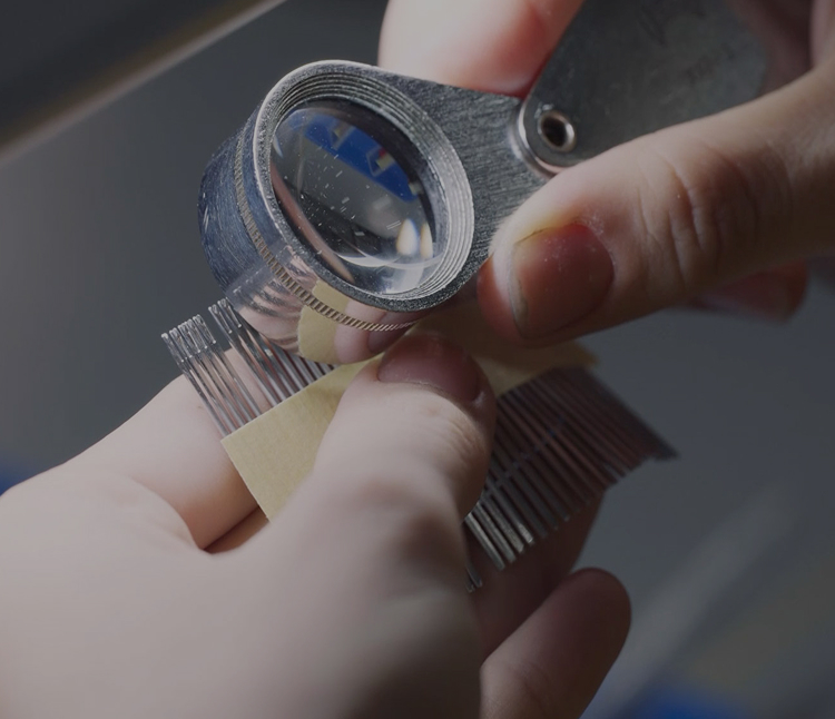 Close-up of a person inspecting fine metal components with a magnifying loupe, focusing on quality contro