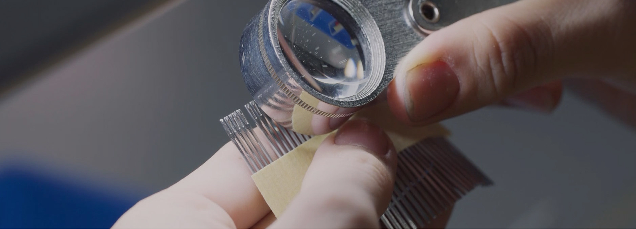 Close-up of a person inspecting fine metal components with a magnifying loupe, focusing on quality contro