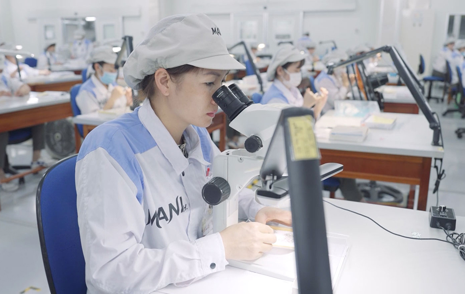 Factory workers in uniform using microscopes at individual workstations for detailed inspection or assembly tasks