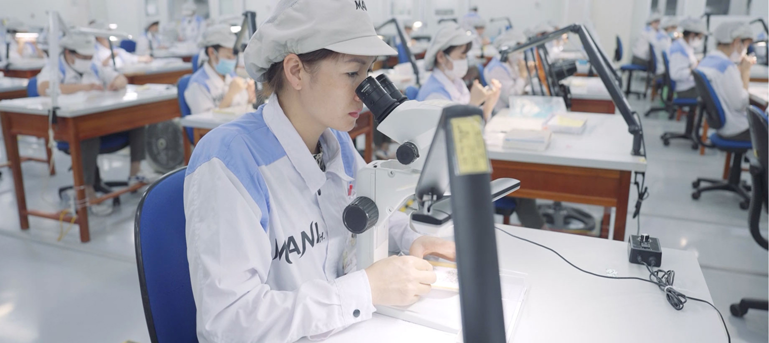 Factory workers in uniform using microscopes at individual workstations for detailed inspection or assembly tasks