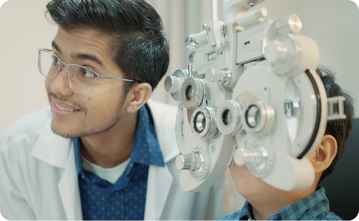An optometrist conducting an eye examination on a child using a phoropter, both smiling and engaged in the process