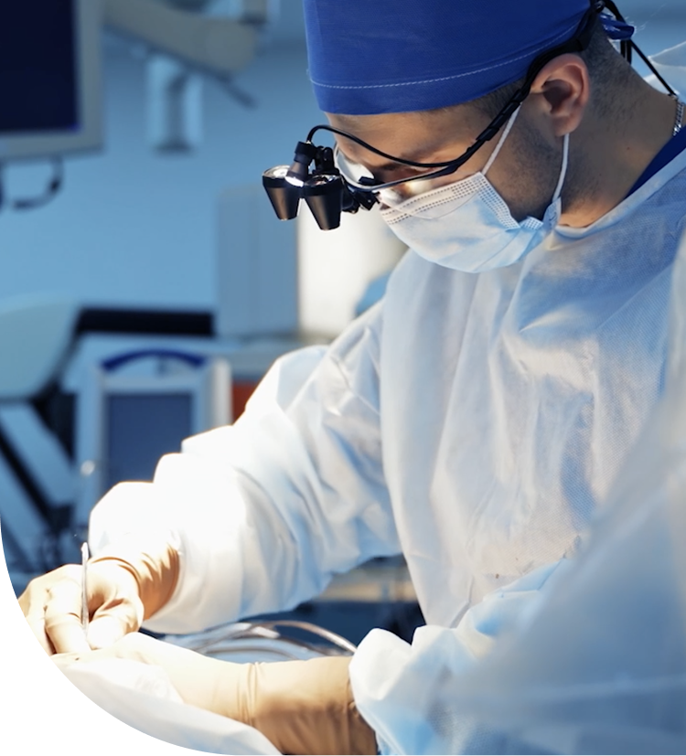 A surgeon wearing magnifying glasses and sterile gown performing a surgical procedure in an operating room