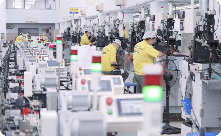 Workers in yellow shirts operating machinery in a large manufacturing or assembly facility